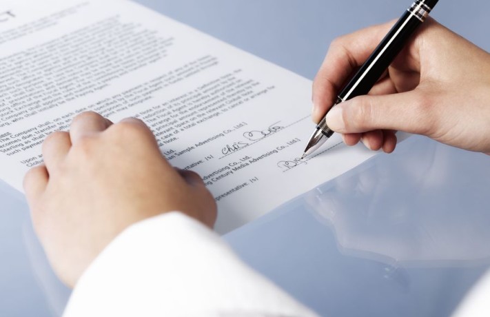 Close up of woman signing a legal document or contract, blank background.
